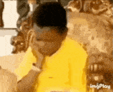 a young boy in a yellow shirt is sitting in a chair with his hand on his chin .