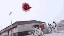 a group of people are standing in front of a building with a red object flying in the sky