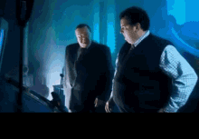 two men standing next to each other in a dark room with a blue light behind them