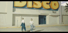a couple of people are standing in front of a disco building .