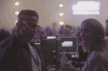 a man and a woman are talking in a dark room with a pink sign in the background that says ' a '