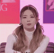 a young woman with pigtails is sitting on a couch with her arms crossed .