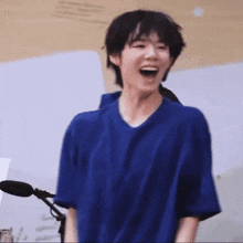 a young man in a blue shirt is laughing in front of a microphone