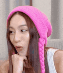 a woman wearing a pink beanie with braids on the ear is making a funny face .