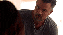 a man with a beard and a gray shirt is looking at a woman .