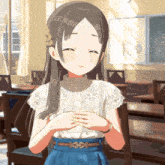 a girl in a white top and blue skirt stands in a classroom with her hands folded