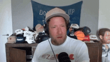 a man wearing a hat and headphones stands in front of a wall that says do it up
