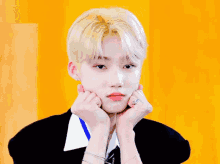 a young man with blonde hair is making a face with his hands on his chin .