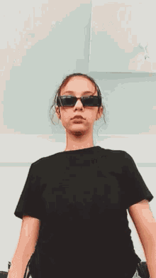 a woman wearing sunglasses and a black crop top is looking at the camera .