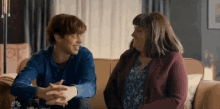 a man and a woman are sitting on a couch and smiling at each other .