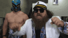 a man with a beard wearing a captain 's hat stands next to another shirtless man