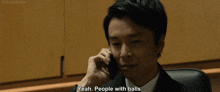 a man in a suit and tie is talking on a cell phone and says " yeah people with balls "