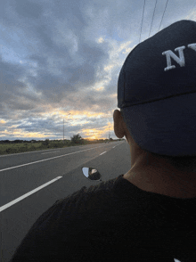 a man wearing a hat with the letter n on it is driving down a highway