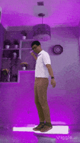 a man in a white shirt and brown pants is standing in front of a purple wall ..