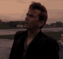 a man in a black suit stands in a field with his mouth open