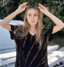 a woman adjusts her sunglasses while wearing a black shirt