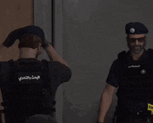 two police officers are standing next to each other in a dark room . one of the officers has arabic writing on his vest