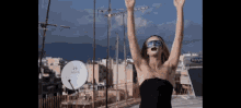 a woman stands on a rooftop with her arms in the air in front of a nova dish