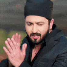 a man with a beard wearing a black hat and a black jacket is clapping his hands