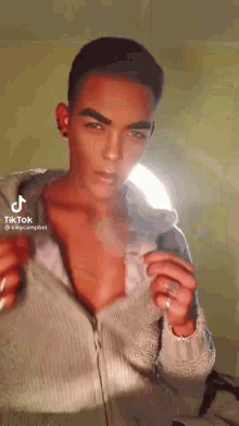 a man is taking off his shirt and looking at the camera while standing in front of a light .