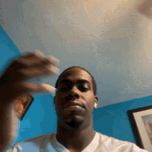 a man wearing ear buds looks at the camera with a blue wall behind him