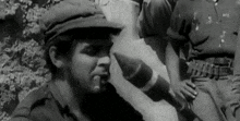 a man in a military uniform is smoking a cigar while holding a bomb in his mouth .