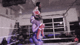 a woman in a red and white outfit is carrying another woman on her shoulders in a wrestling ring