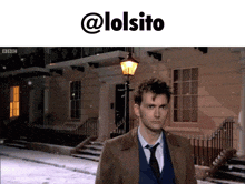 a man in a suit and tie is walking down a snowy street with a lamp post in front of him