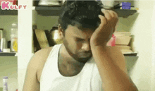 a man in a white tank top is holding his head in his hands .