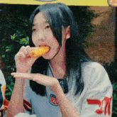a girl wearing a white shirt with the number 21 on it is eating a fried food item .