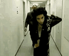 a man in a black jacket is walking down a hallway with a man in a suit .