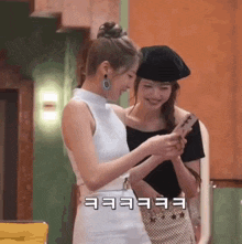 two women are standing next to each other and one is holding a cell phone