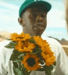 a man wearing a green hat is holding a bouquet of sunflowers around his neck .