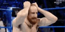a man with a beard is in a wrestling ring with his hands on his head .