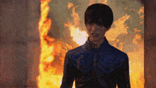 a man in a blue jacket stands in front of a large fire