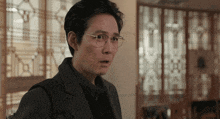 a man wearing glasses and a suit is standing in front of a window with chinese writing on it