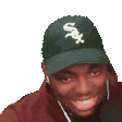 a man wearing a white sox hat and earphones is smiling .