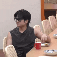 a man wearing glasses sits at a table with a red nescafe mug