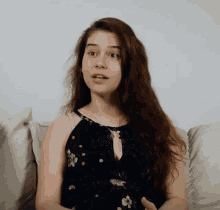 a woman sitting on a couch wearing a black floral dress