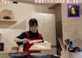 a woman in a red apron is cutting onions on a cutting board in front of a tv screen
