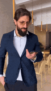 a man with a beard wearing glasses and a blue jacket is looking at his phone