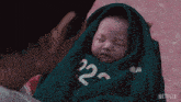 a man is holding a baby wrapped in a green sweater with the number 22 on it