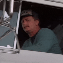 a man is sitting in the driver 's seat of a truck and looking out the window .