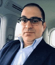 a man in a suit and glasses is sitting in a car