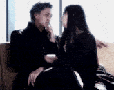 a man and a woman are sitting on a couch and the woman is touching the man 's face