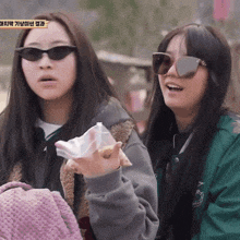 two girls wearing sunglasses are standing next to each other and one is holding a piece of paper in her hand