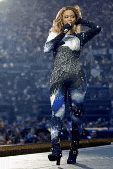 a woman in a blue and white jumpsuit is singing into a microphone while standing on a stage