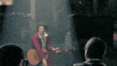 a man in a red suit is holding a guitar in front of a crowd