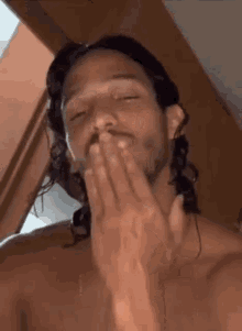 a shirtless man with long hair is blowing a kiss .