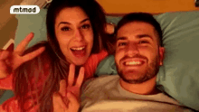 a man and a woman are laying on a bed and the woman is giving the peace sign